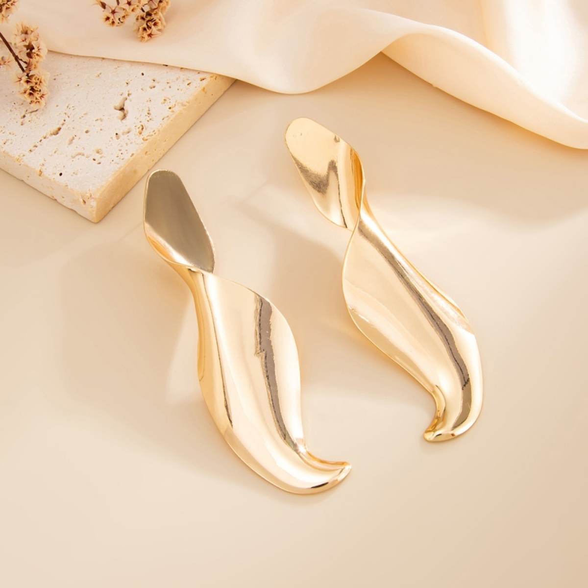 Pair of Soleil sculptural gold-tone drop earrings with a polished twisted silhouette, displayed on a cream background.