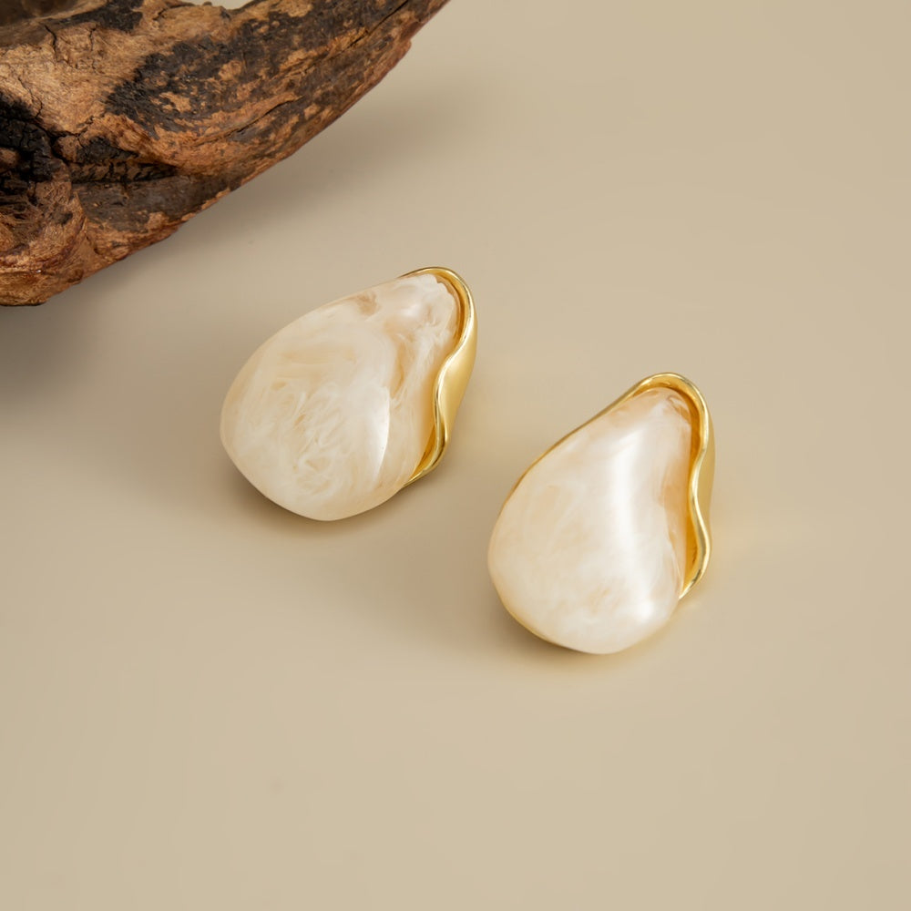 Pair of Perla cream marbled teardrop earrings with curved gold-tone edging on a beige background.