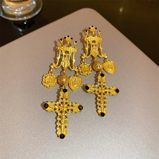 Gold cross earrings with intricate designs on a light background