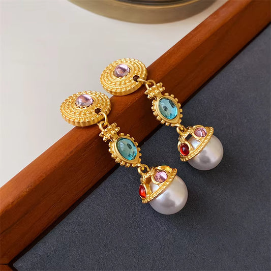 Gold earrings with pearls and gemstones on a dark surface