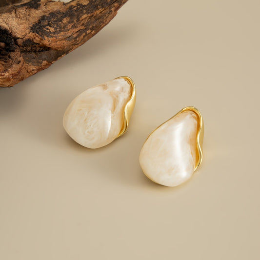 Pair of Perla cream marbled teardrop earrings with curved gold-tone edging on a beige background.