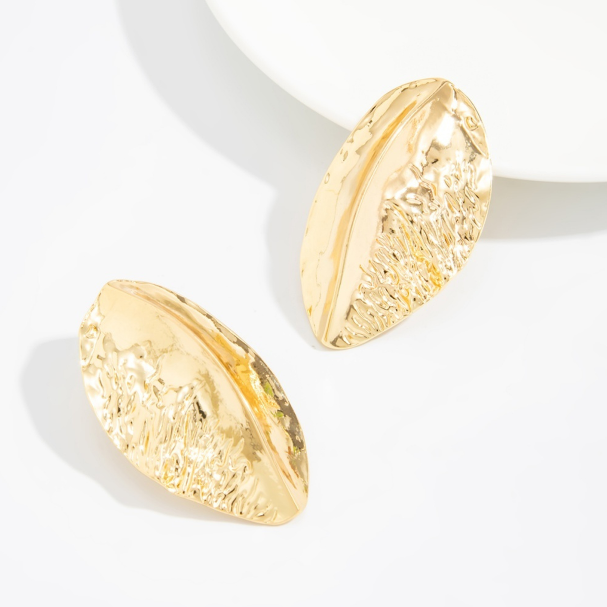 Pair of Alba gold-tone statement stud earrings with sculptural, leaf-like curves and hammered texture on a white background.